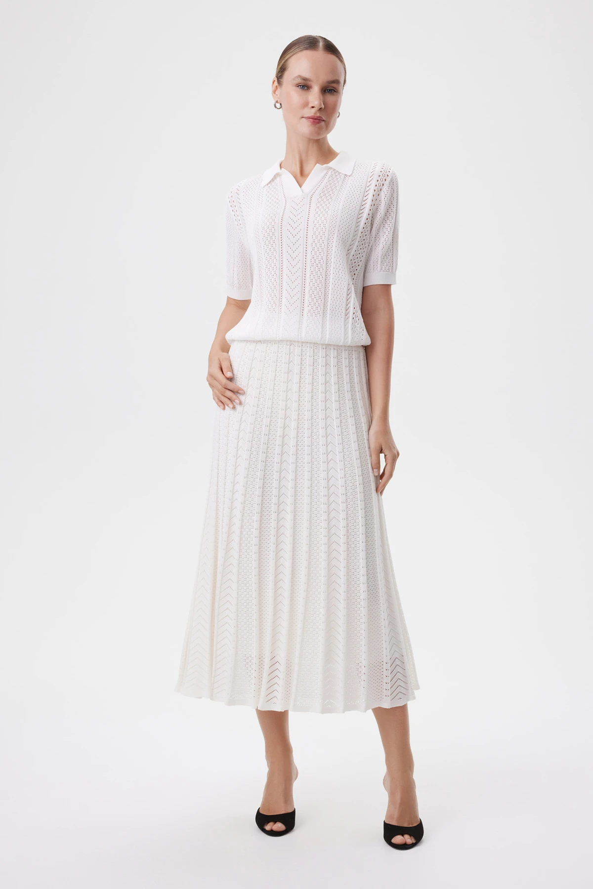 Полный образ из белого трикотажного топа и плиссированной юбки на чистом студийном фоне.